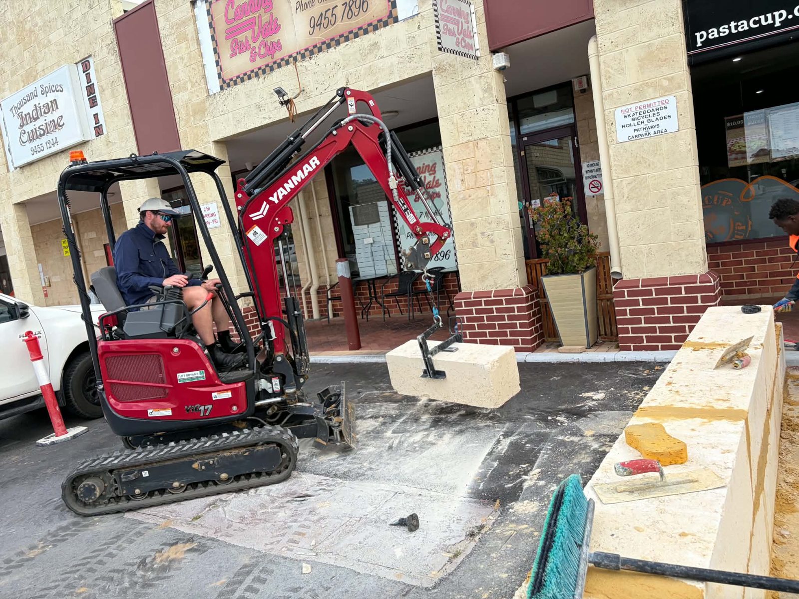 TNI Yanmar ViO17-1 with the limestone block lifter carrying a 250kg block to a retaining wall outside shops in Canning Vale, Perth
