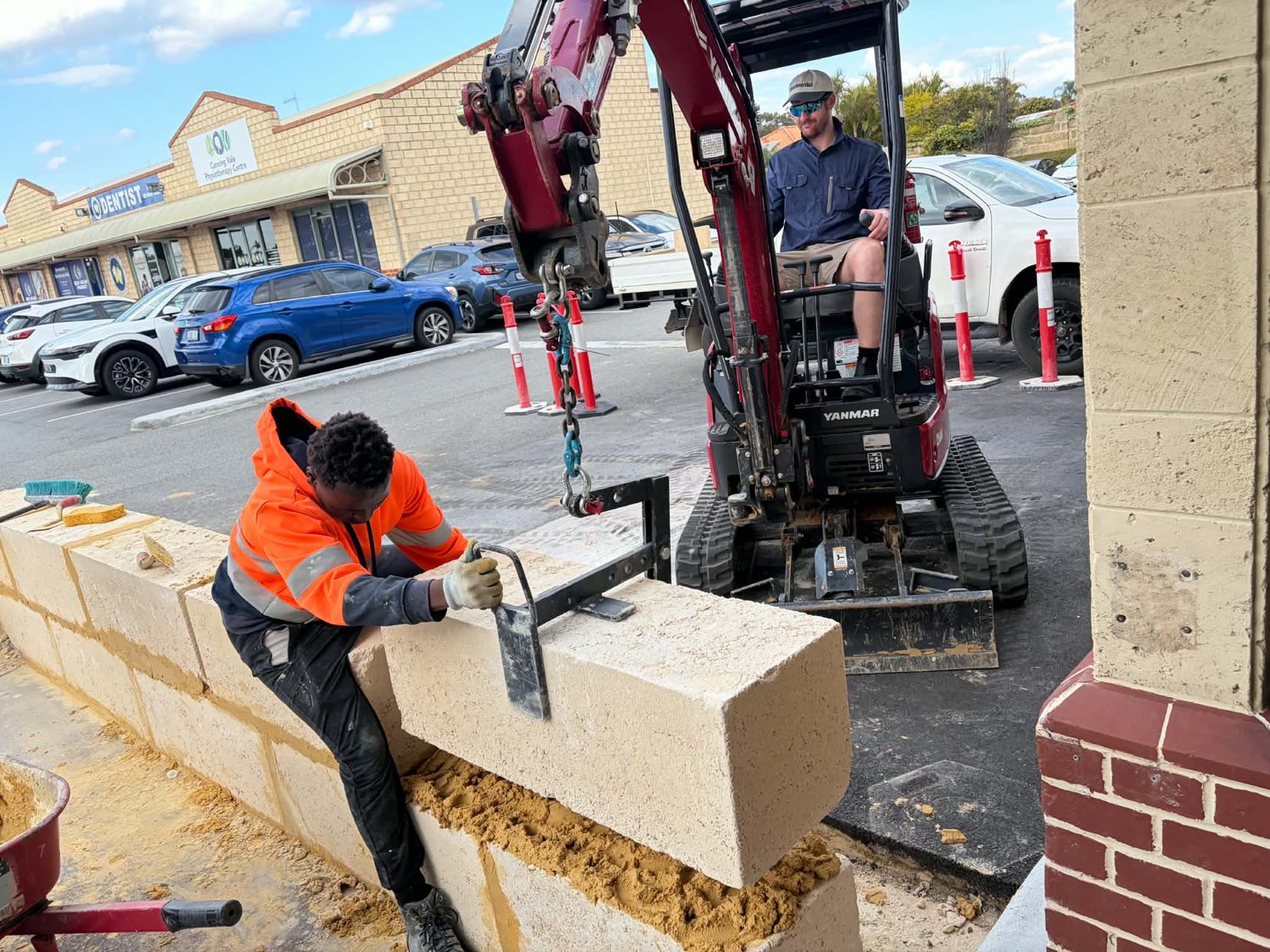 Limestone block being guided onto the wall course with the block lifter while the excavator holds it level